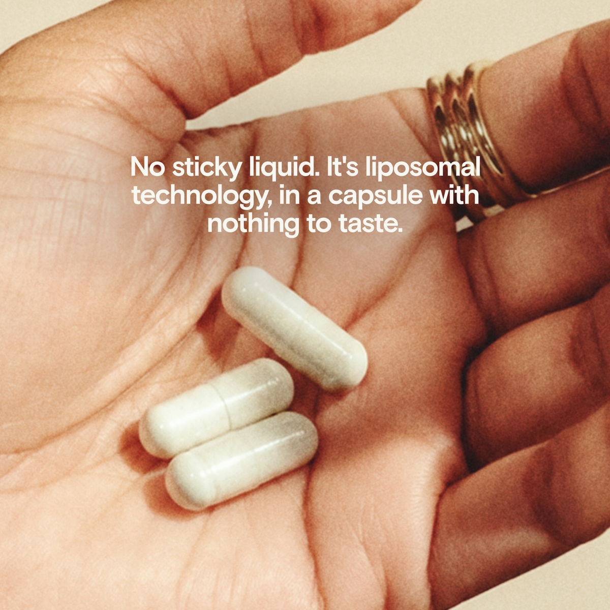 A close-up of an open hand holding three white liposomal capsules, with white text overlay reading: 'No sticky liquid. It's liposomal technology, in a capsule with nothing to taste.
